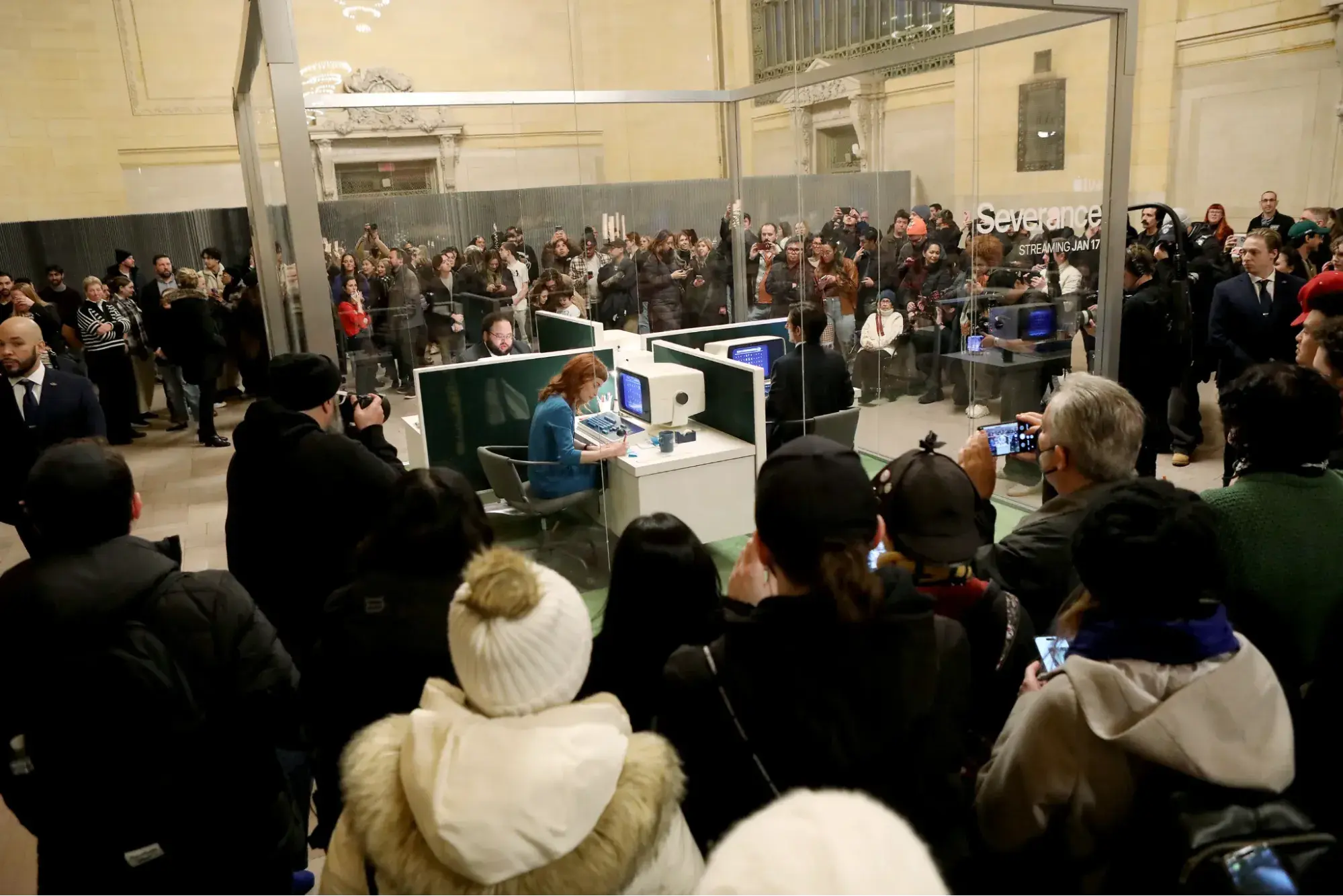 a photo of the severance pop-up glass box in grand central station with a crowd of spectators surrounding
